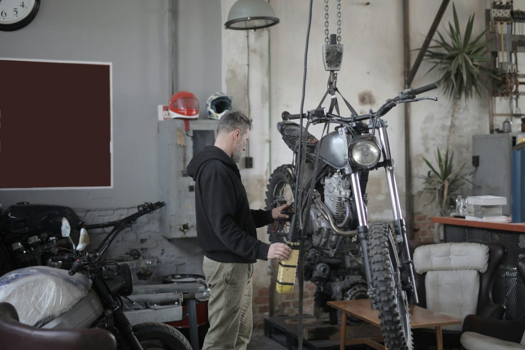 Mechanic working on a motorcycle in an industrial workshop, performing maintenance tasks.